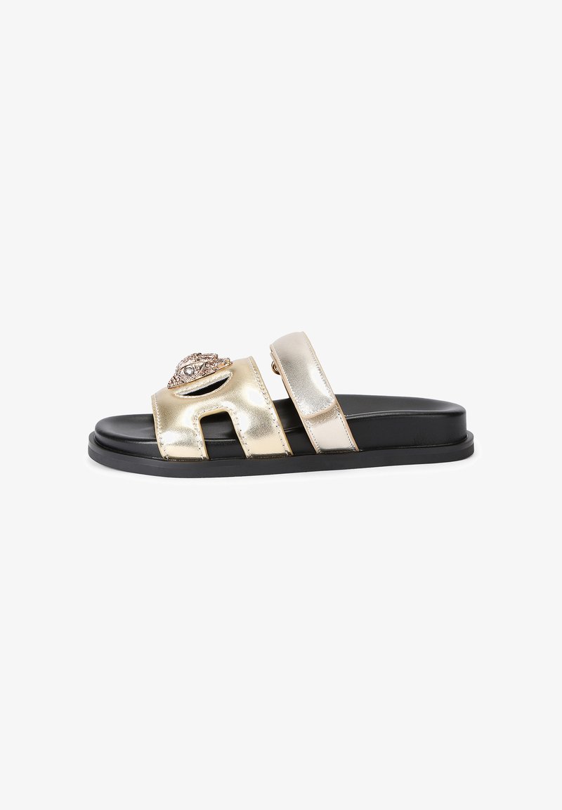 Black sole slide sandal with two metallic gold straps, one featuring a rhinestone-studded decorative eye-shaped emblem.