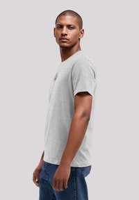 Gray cotton t-shirt with a classic crew neckline, short sleeves, and a subtle black logo detail on the chest. Worn with blue denim jeans.