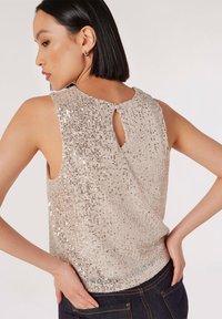 Top beige con paillettes e apertura a chiave, caratterizzato da un collo tondo e design senza maniche. La texture è lucida con una finitura liscia.