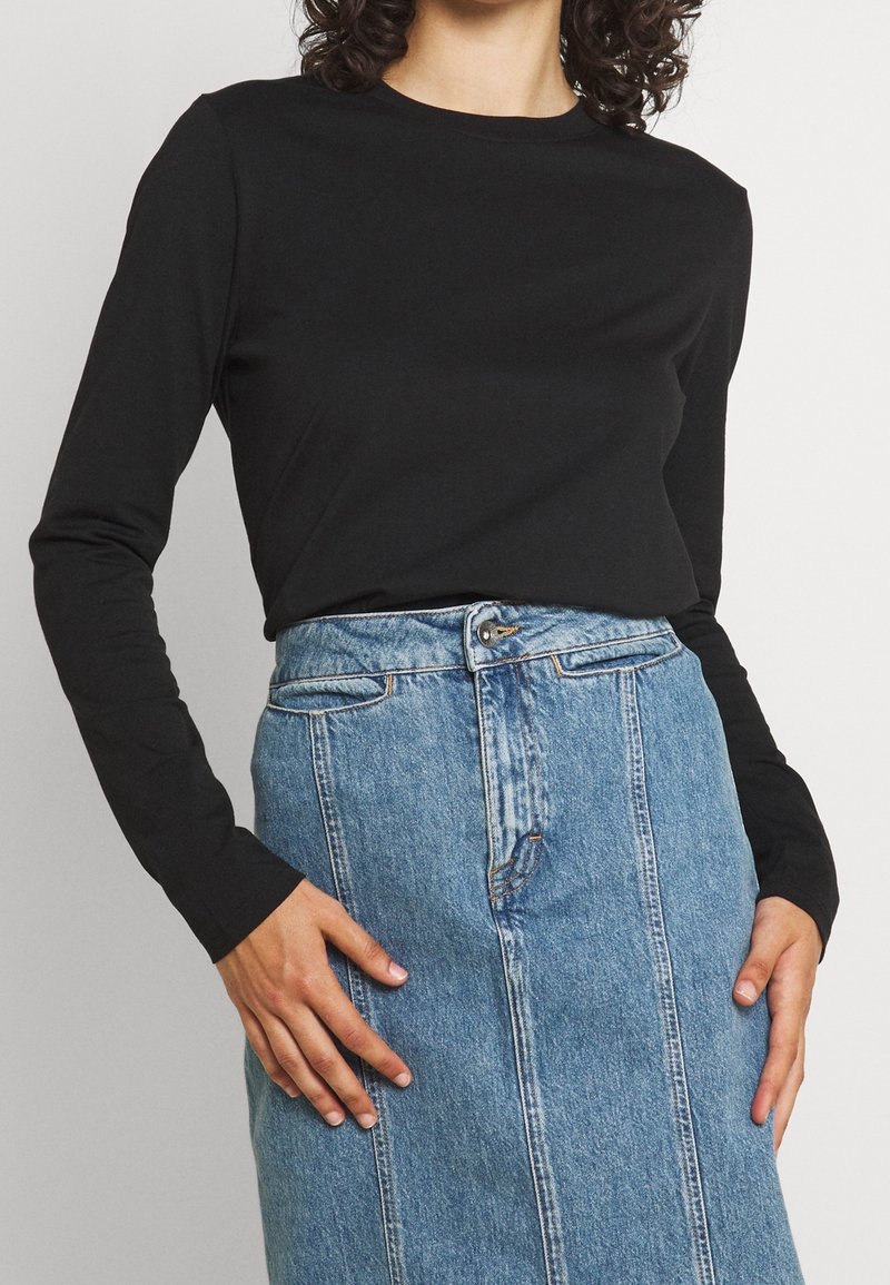 Svart långärmad skjorta i kombination med en blå jeanskjol med frontknappar och dragkedja, synlig söm och rakt snitt.