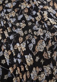 Falda de tela negra con pliegues y un patrón floral en beige y azul claro. Presenta pequeños botones y una superficie texturizada.