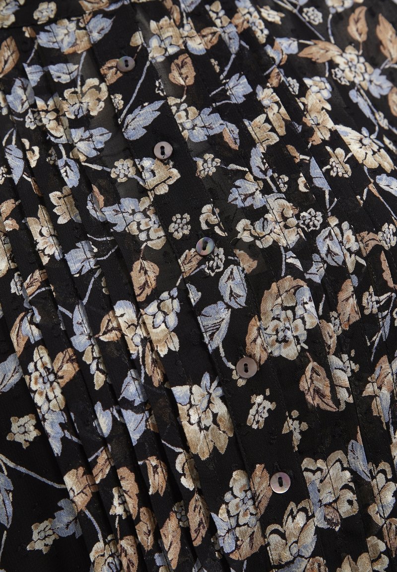 Falda de tela negra con pliegues y un patrón floral en beige y azul claro. Presenta pequeños botones y una superficie texturizada.