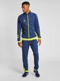 Marinträningsdräkt med limegröna accenter; zip-up jacka med prickig mönster och logotyp; matchande byxor, sportig design, tyg med lätt glans.