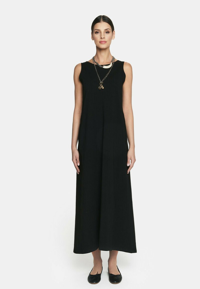 Czarna, bezrękawnikowa sukienka maxi o zwiewnej sylwetce, z okrągłym dekoltem i warstwowym naszyjnikiem. Noszona z czarnymi płaskimi butami.