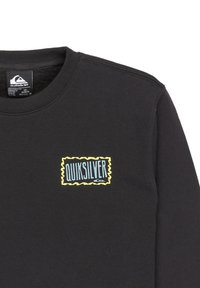 Chemise noire à manches longues avec col côtelé; présente un logo Quiksilver rectangulaire en bleu et jaune sur la poitrine gauche. Matière en coton doux.