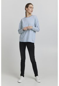 Világoskék és fehér csíkos, laza szabású, hosszú ujjú ing, fekete, skinny farmernadrággal és fehér sportcipővel párosítva.