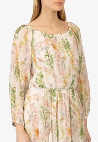Blouse à imprimé floral avec un décolleté carré, des manches longues et des poignets élastiques. Fabriquée en tissu léger et transparent dans des couleurs pastel.
