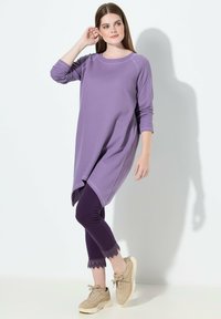 Fioletowa tunika z długim rękawem, zaokrąglonym dołem, w duecie z ciemnofioletowymi legginsami ozdobionymi koronką. Dopełnieniem stroju są beżowe trampki.