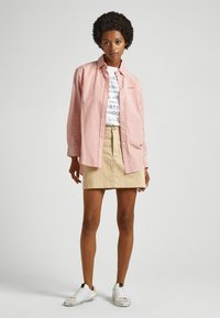 Camicia a righe rosse e bianche sopra una t-shirt bianca con grafica, abbinata a una minigonna beige e sneaker bianche.