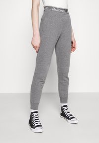 Grå sweatpants med elastisk midja som har "Hollister"-logotyp, design med smalare ben och ribbade muddarna, tillsammans med svarta hög-top sneakers.