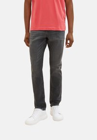 Graue Denim-Jeans mit slim Fit, die eine glatte Textur und minimale Nähedetails aufweisen, kombiniert mit weißen Sneakers und einem rosa Hemd.