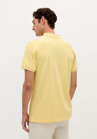 Polo shirt i lys gul, korte ærmer, klassisk krave, blødt bomuldsstof, sideslidser i kanten og en afslappet pasform.