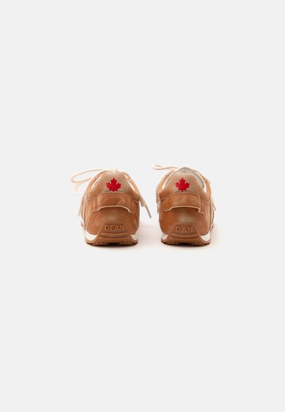Paire de baskets en cuir marron clair avec des lacets, feuille d'érable rouge sur le talon, et noms "DEAN" et "DAN" embossés sur les bords de la semelle.
