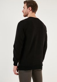 Black sweatshirt with long sleeves, round neckline, and ribbed cuffs. Smooth texture, fitted design, and a straight hemline.