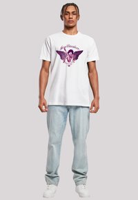 White cotton t-shirt featuring a purple graphic design of a winged character with the word "Heartbreaker." Worn with light blue jeans and white sneakers.