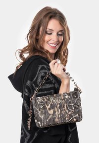 Bolso de mano texturizado en negro y beige con un diseño ondulado, correa de cadena y acentos metálicos. Presenta un logo grabado y un charm decorativo.