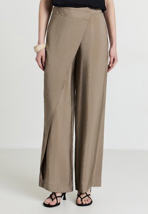 Pantaloni beige a gamba larga con finitura testurizzata, caratterizzati da un design avvolgente e una vita alta. Abbinati a sandali neri con lacci.