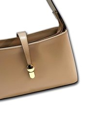 Sac à main en cuir beige au design structuré, doté d'une sangle plate et d'un détail de fermoir doré à l'avant.