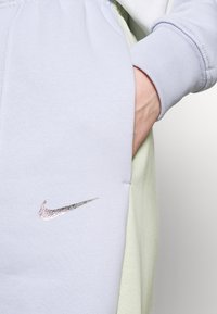Pantalon de survêtement bleu clair en tissu doux, avec un logo swoosh Nike argenté et une poche latérale ; taille élastique et poignets élastiques.