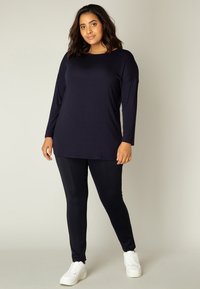 Navy longsleeve top met een relaxte pasvorm; gecombineerd met zwarte legging en witte platform sneakers. Gladde stofstructuur, eenvoudig ontwerp.