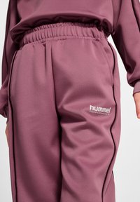 Lilla træningsbukser med elastisk talje, med en glat tekstur og et hvidt "hummel PERFORMANCE" logo på siden.