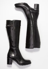 Botas altas de cuero negro hasta la rodilla con un tacón grueso, cremallera lateral y detalle de correa en el tobillo. Textura suave con una suela resistente.