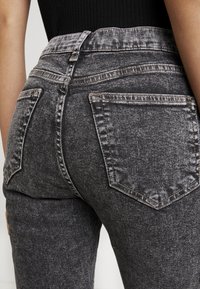 Primer plano de una persona que viste jeans de mezclilla de tiro alto, con un lavado ácido negro, y un top negro acanalado.