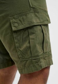 Pantalones cortos cargo verde oliva hechos de tela de algodón, con bolsillos laterales y un corte holgado, dobladillos cosidos y textura suave.