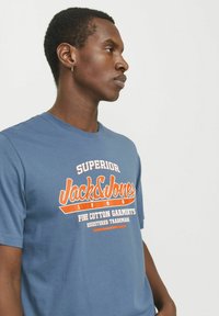 Blauwe katoenen t-shirt met oranje grafische tekst "Jack & Jones" en logo. Ronde halslijn en korte mouwen in een comfortabele pasvorm.