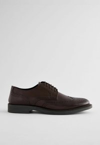 Chaussure oxford en cuir marron avec un design à bout d'aigle, des détails perforés, un bout rond et une semelle noire. Lacets à l'avant pour un maintien sécurisé.