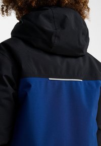 Veste imperméable avec une capuche noire et une partie supérieure noire, se dégradant en un corps bleu vif avec une bande réfléchissante près du col.