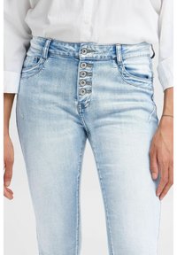 Jeans de denim de color azul claro con una cintura alta, que cuentan con un cierre de cinco botones, bolsillos frontales y un ligero desgaste para dar textura.