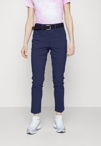 Marineblaue Hose mit schlanker Passform und schmal zulaufenden Knöcheln, kombiniert mit einem schwarzen Gürtel. Tragen Sie dazu ein pinkfarbenes Batik-T-Shirt und graue Sneakers.