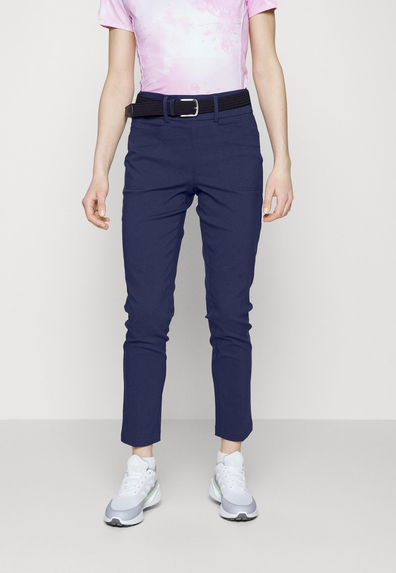Marineblaue Hose mit schlanker Passform und schmal zulaufenden Knöcheln, kombiniert mit einem schwarzen Gürtel. Tragen Sie dazu ein pinkfarbenes Batik-T-Shirt und graue Sneakers.