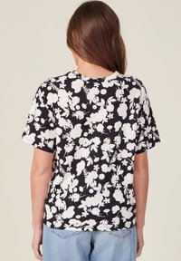 Camiseta negra con patrón floral blanco, de mangas cortas y cuello redondo. Tejido suave con un corte holgado y una textura sutil.