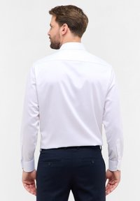 Collo bianco a maniche lunghe con una trama liscia, caratterizzato da un colletto classico e polsini con bottoni, abbinato a pantaloni blu navy e una cucitura posteriore discreta.