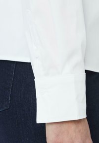 Weißes Langarmhemd mit Knopfmanschette, ausgestattet mit einer glatten Textur und taillierter Passform, kombiniert mit dunkler Jeans.