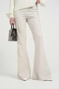 Beige bukser med vidde og en glat tekstur, iført med en cremefarvet sweater. En lille brun håndtaske, der holdes i hånden, har et struktureret design.