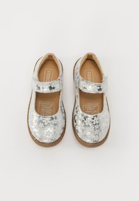 Silberne Mary Jane Schuhe mit floralem Muster, abgerundeter Spitze, verstellbarem Riemen und einem Innenfutter aus hellbraunem Leder. Braune Gummisohle.