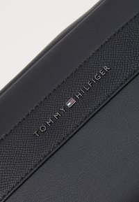 Svart lærveske med teksturert overflate. Preget "TOMMY HILFIGER"-logo med en fargetone. Strømlinjeformet, rektangulært design.