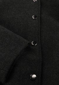 Zwarte herringbone wollen jas met een gestructureerde stof, grote zwarte knopen en een omgeslagen mouw met een nette afwerking.