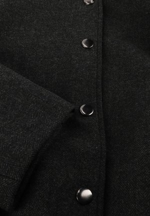 Zwarte herringbone wollen jas met een gestructureerde stof, grote zwarte knopen en een omgeslagen mouw met een nette afwerking.