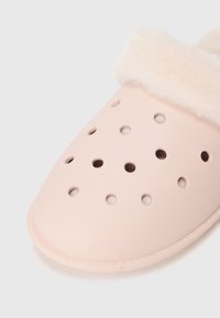 Chausson rose clair avec plusieurs trous de ventilation et un doublure moelleuse de couleur crème autour de l'ouverture.