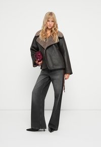 Sort læderjakke med en brun fleecekrave, parret med højtaljede mørkegrå flagrende jeans. Modellen holder en lilla håndtaske.