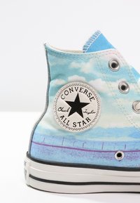 Tenisky Converse All Star s vysokým střihem, vzor modré oblohy a mraků, bílý kruhový logo a stříbrné oky.