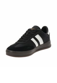 Zapatilla negra con parte superior de ante y sintético, dos franjas blancas, suela gruesa gris y cordones negros para un ajuste seguro.