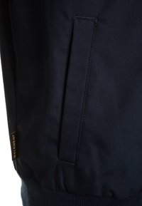 Giacca navy con tessuto testurizzato, vita aderente e tasca laterale con cucitura nascosta. Logo Element visibile vicino all'orlo.