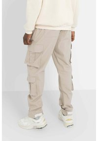 Beige cargobroek met meerdere zijzakken, gemaakt van een katoenmix, met een tapering fit, voorzien van een manchettenzoom en gecombineerd met witte sneakers.