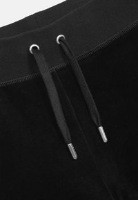 Crne baršunaste trenirke s crnim elastičnim pojasom, koje imaju srebrne metalne rupice i kordice za zatezanjem. Glatka tekstura i mekani završetak.