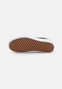 White sneaker sole with a textured honeycomb design in brown rubber, featuring a curved white edge. Minimalist and functional appearance.